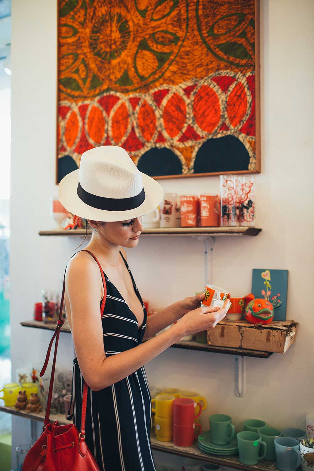 woman in hat and black stripe dress holding a cup inside a boutique