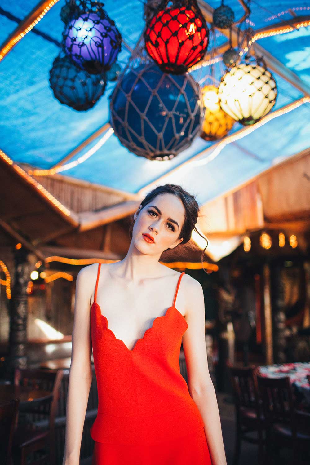 woman in sleeveless red dress standing under colorful glass lanterns