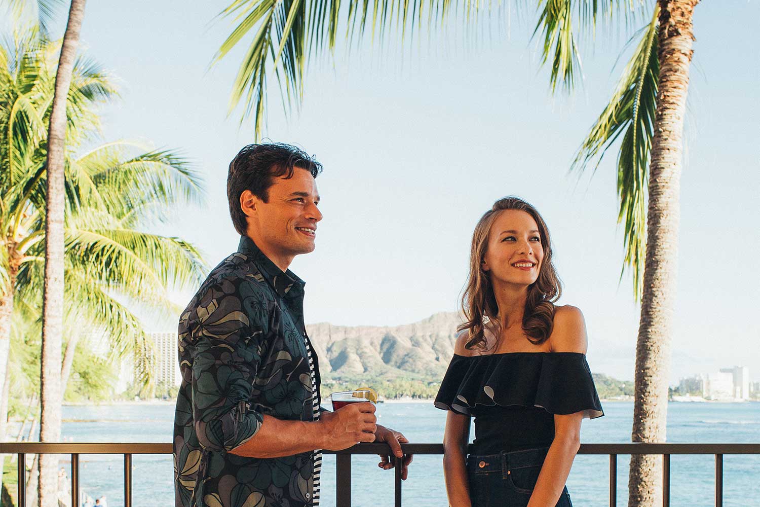 man and woman standing on hotel balcony with palm trees and Diamondhead in background