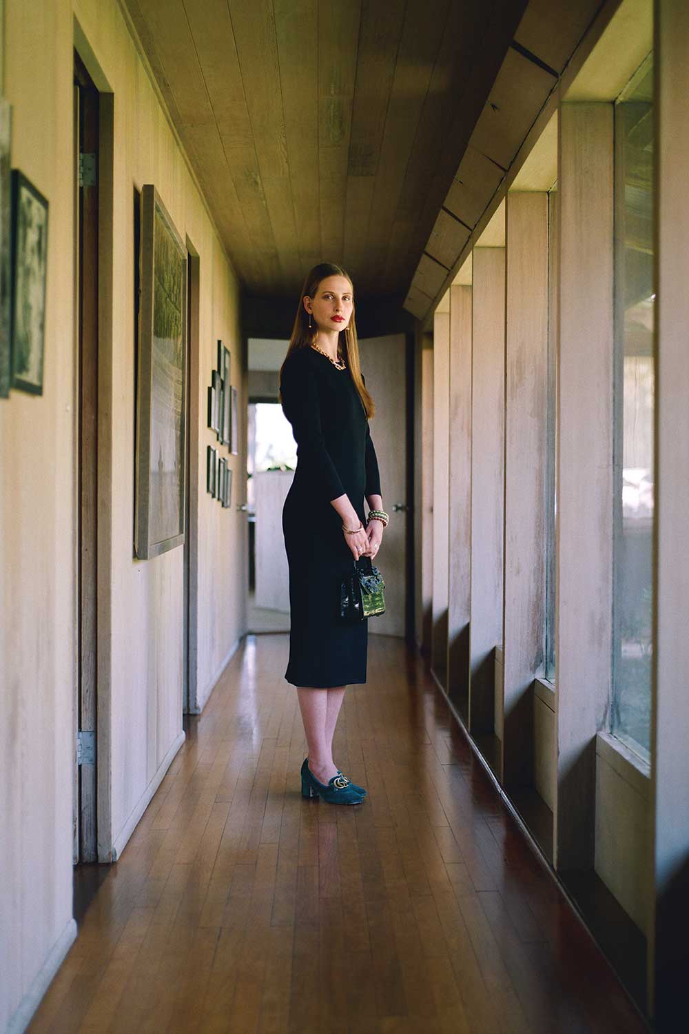 Woman in black dress standing in hallway holding small bag