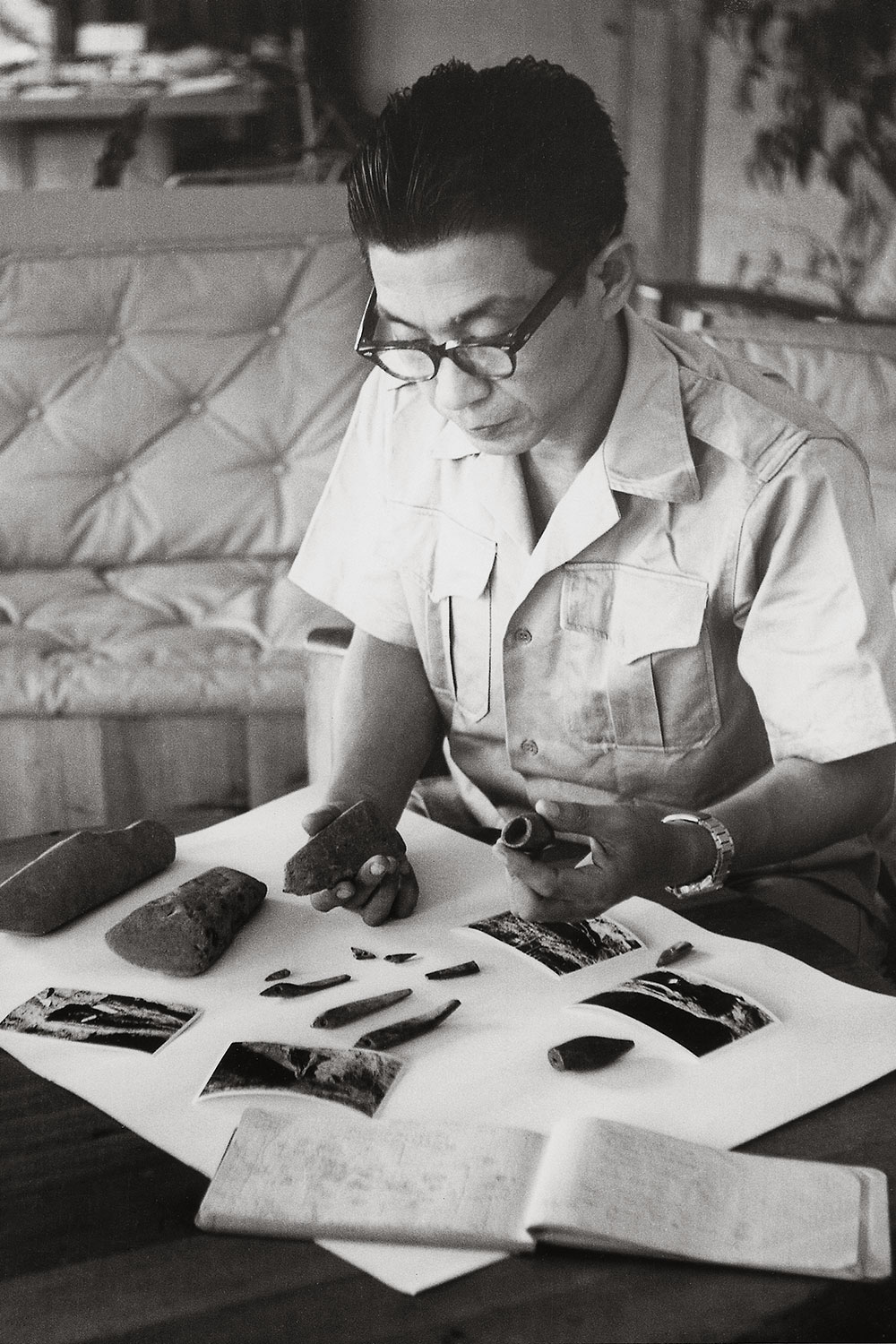 Black and white image of an asian man with glasses examining artifacts.