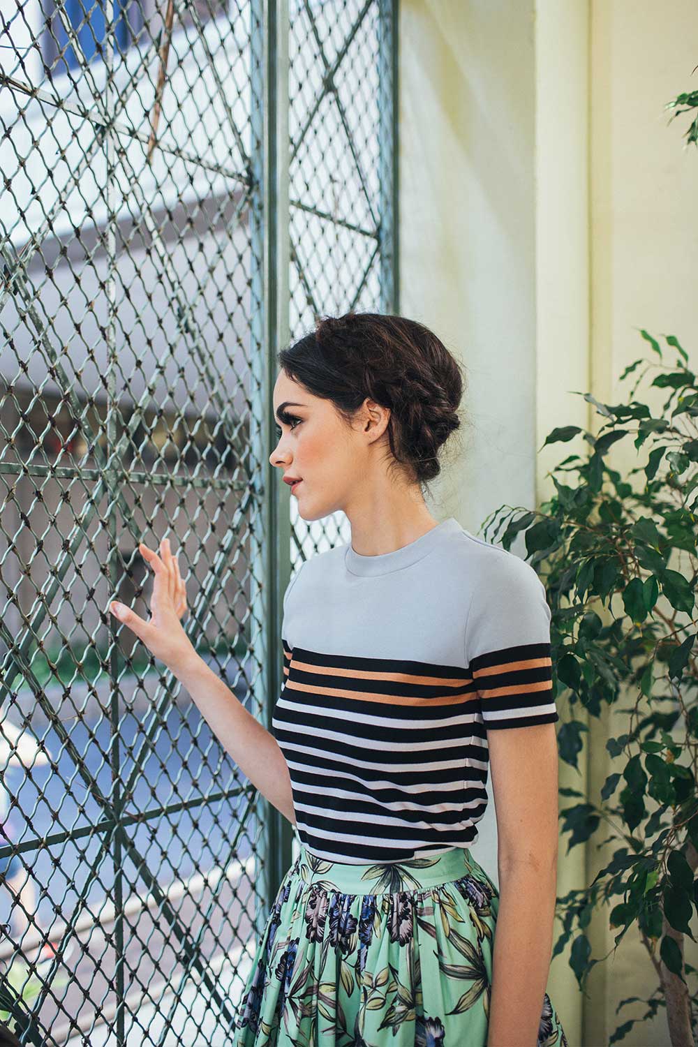 woman in striped shirt and flowered skirt with hand on chain link fence