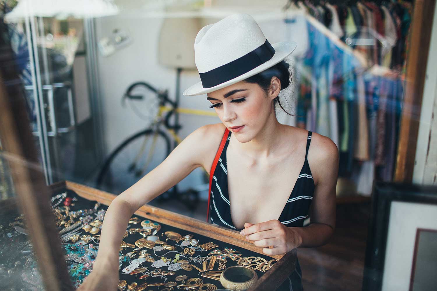 Woman in white hat and black striped dress looking at vintage jewelry