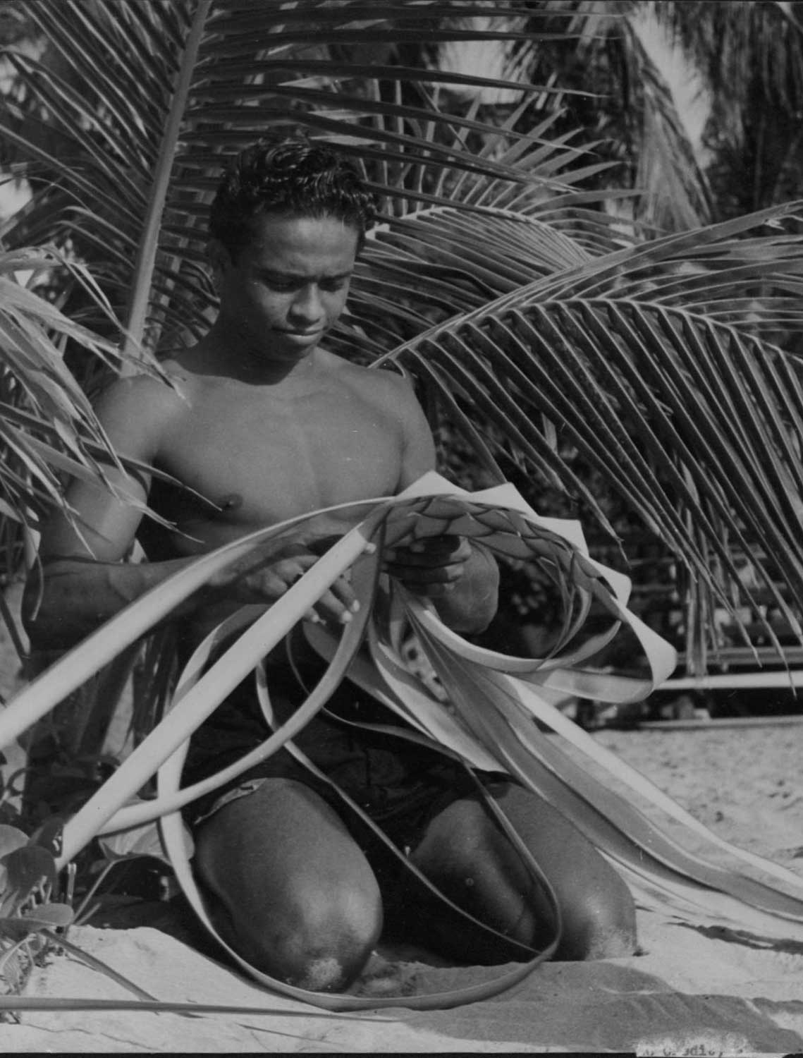 Black and white developed image of man weaving with coconut leaves.